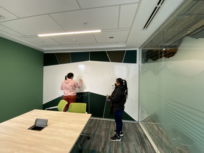 Una sala de reuniones con una paredes con diseños verdes con pintura pizarra - 2 mujeres